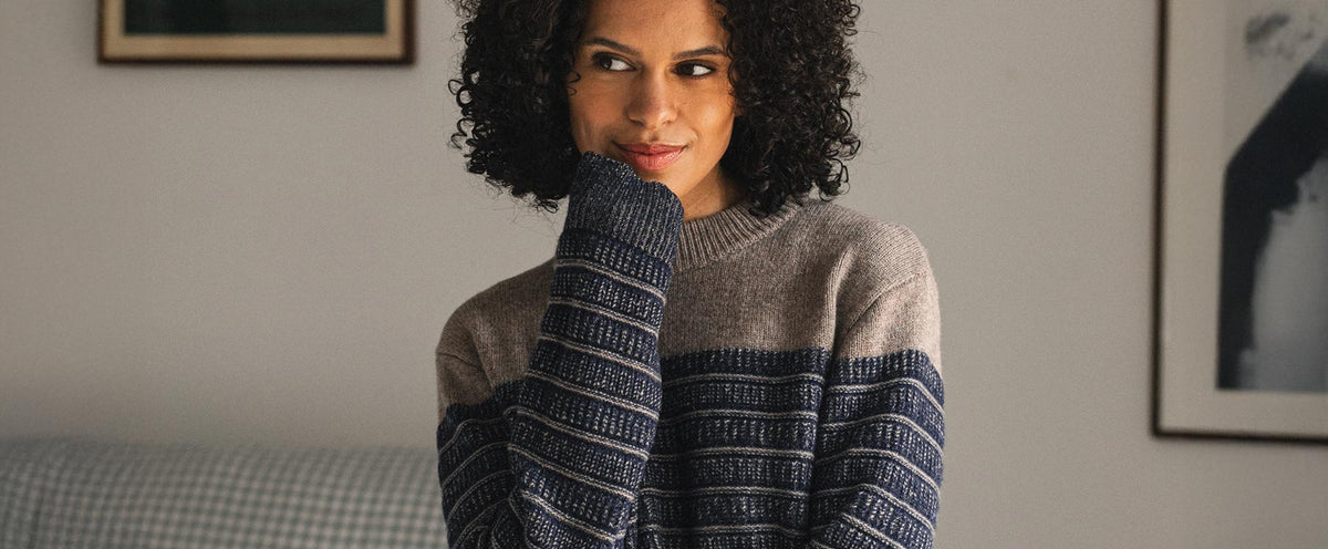 A woman with curly hair wears a beige and navy blue striped sweater.