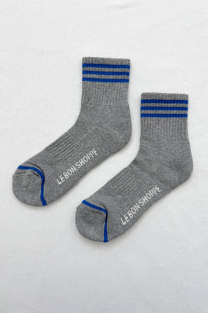 Le Bon Shoppe - Girlfriend Socks in grey feature two blue stripes near the top, blue toe accents, and “LE BON SHOPPE” in white on the soles—women’s crew socks combining style and comfort, shown flat on a white background.