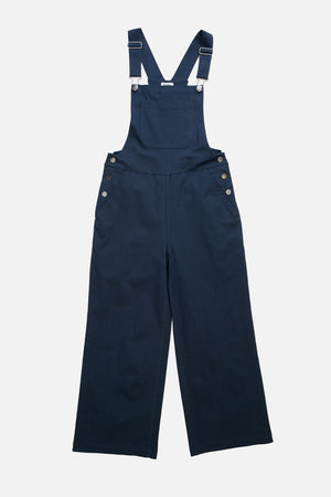 The Bridge & Burn Roscoe Overall in navy canvas features wide legs, adjustable shoulder straps, a front bib, and silver side buttons, made from cotton canvas and shown laid flat on a white background.