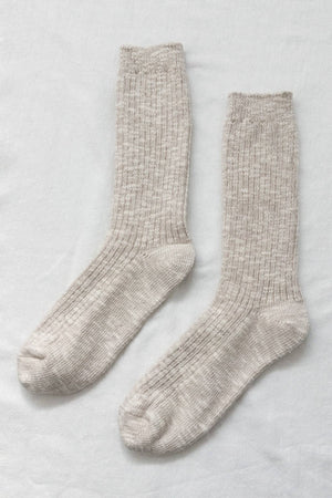 A pair of Le Bon Shoppe Cottage Socks in Oatmeal, featuring a chunky knit in light beige, laid flat side by side on a white fabric background.