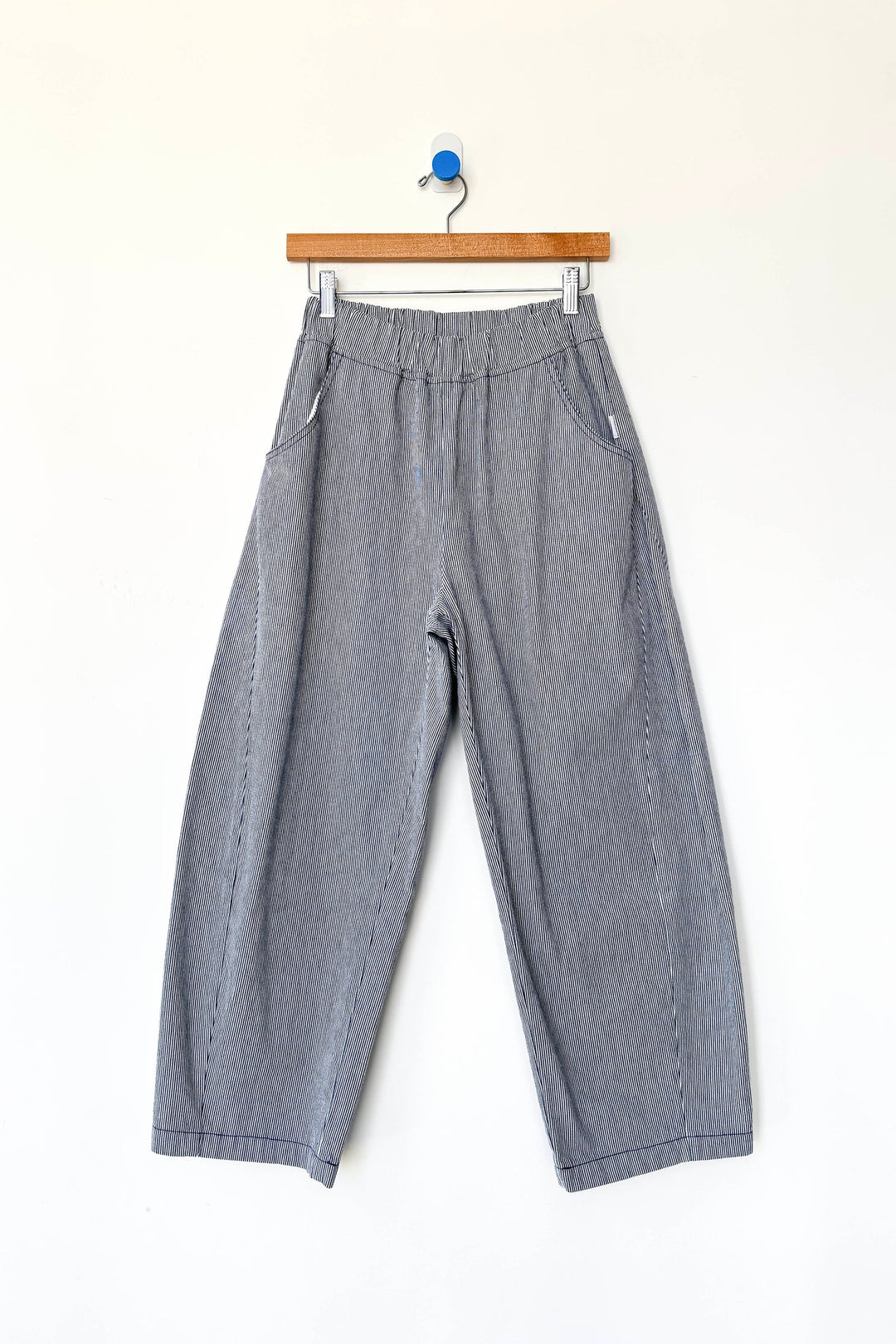 Le Bon Shoppe - Arc Pant in Blue Stripe features a wide-leg silhouette with an elastic waistband and convenient side pockets, crafted from heavyweight canvas for lasting durability. Displayed on a wooden hanger against a clean white background, these stylish everyday pants by Le Bon Shoppe are perfect for elevated comfort and style.