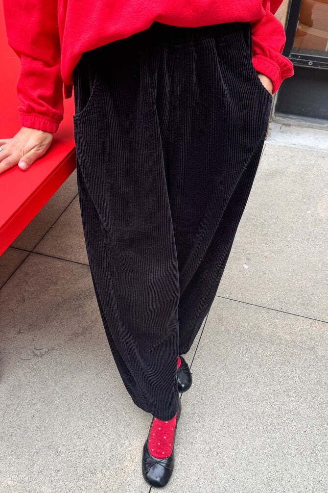 Le Bon Shoppe Soft Corduroy Arc Pant in black, featuring a cropped length and elastic high waist, styled with red socks and black ballet flats.