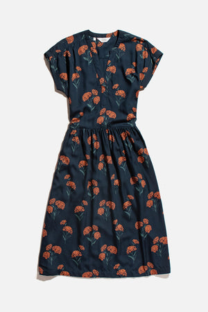 The Bridge & Burn Ira Dress / Wildflower is a navy blue knee-length modal pullover with short sleeves, a V-neckline, an elastic waist, and an orange and green floral print. Shown laid flat on a white background.
