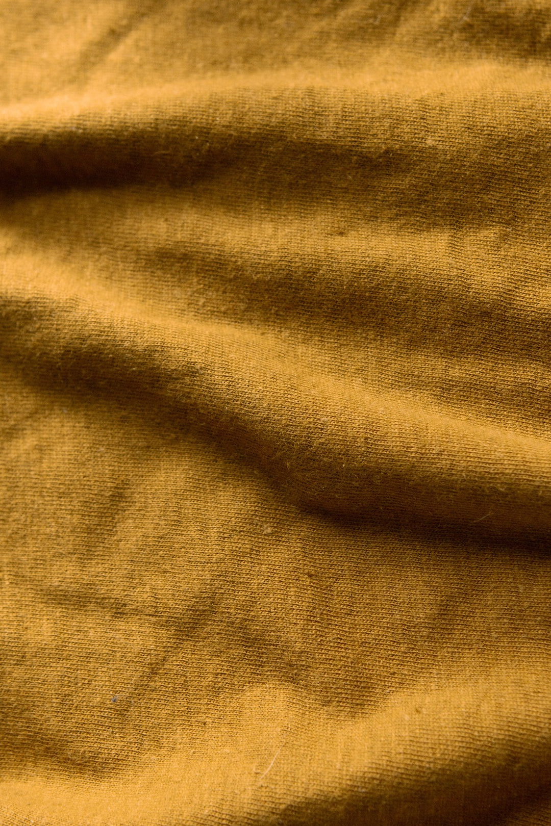 A close-up of the Organic Hemp Pocket Tee in ochre by Bridge & Burn reveals its woven texture and soft folds—perfect for a sustainable t-shirt made from organic cotton and hemp.