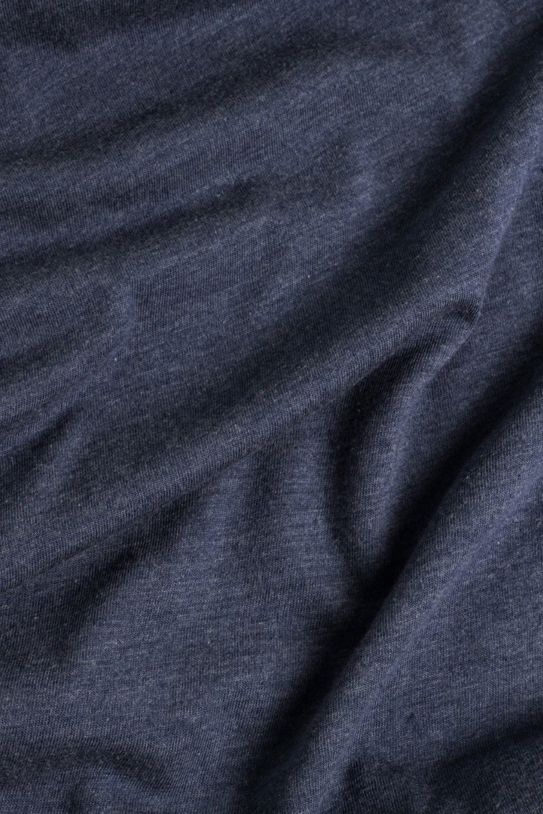 Close-up of the Women's Alpenglow Tee in Navy by Bridge & Burn, featuring dark gray heathered fabric made from recycled polyester, with gentle folds highlighting its soft, smooth, and subtly textured surface.