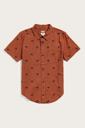 The Bridge & Burn Malcolm Shirt in Rust Fil-Coupé Pyramids is an organic cotton, short-sleeve button-up with a collar and front pocket, featuring a small black pyramid pattern. Laid flat on a white background.