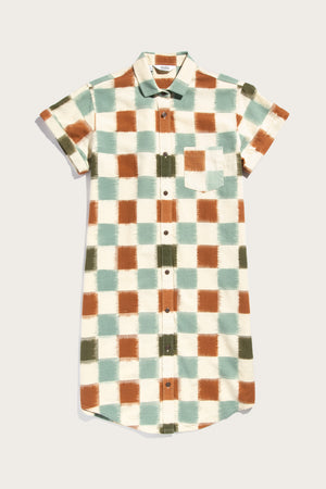 The Loren Shirt Dress / Mod Checker by Bridge & Burn is a 100% cotton, short-sleeve dress with a collar and chest pocket, featuring a painted-style checkered pattern in green, brown, blue, and off-white.