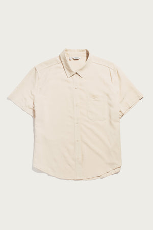 The Bridge & Burn Greer Cropped Shirt in cream is a light beige, boxy short-sleeve button-up with a collar and single chest pocket, made from soft twill and shown laid flat on a white background.