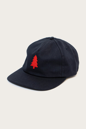 The Bridge & Burn Tree Cap / Navy is a cotton twill hat with a small red embroidered pine tree on the front and a leather adjustable strap, shown against a neutral background.
