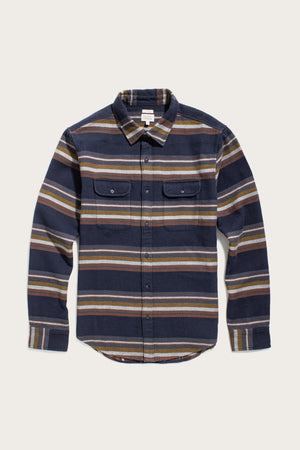 The Bridge & Burn Cole Slim Shirt in Coastline Stripe is a navy blue, slim fit long-sleeve with beige, brown, and olive green horizontal stripes, button-down front, and two chest pockets with button flaps.