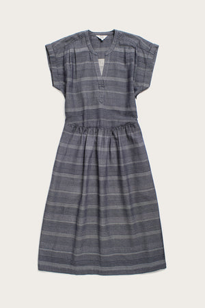 The Bridge & Burn Ira Dress in Cascade Weave is a short-sleeve, knee-length organic cotton dress with subtle gray stripes, V-neckline, gathered waist, and a relaxed pullover fit for effortless comfort.