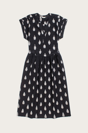 The Ira Dress in Eclipse Ikat by Bridge & Burn is a black, knee-length pullover with short dolman sleeves, V-neck, and gathered waist. It features an abstract white dotted pattern and is displayed flat on a white background.