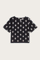 The Bridge & Burn Leona Shirt in Eclipse Ikat features short sleeves, a boxy fit, round neckline, and an evenly spaced white abstract pattern on black fabric. Displayed flat on a white background.