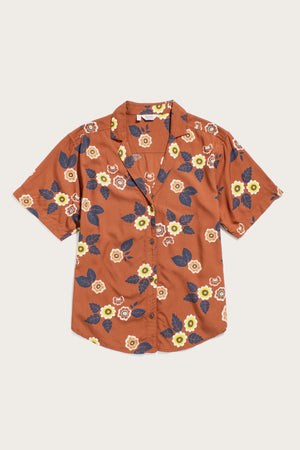 The Bridge & Burn Mila Cropped Shirt in Rose Floral is a short-sleeve, button-up featuring a rust background with yellow, white, and navy flowers. Crafted from breathable modal, it offers a relaxed fit and notched collar.