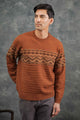 A man with short dark hair wears the Bridge & Burn Rockwood Fairisle Sweater in Walnut Grove, featuring a geometric chest pattern, paired with gray pants and standing against a textured gray background.