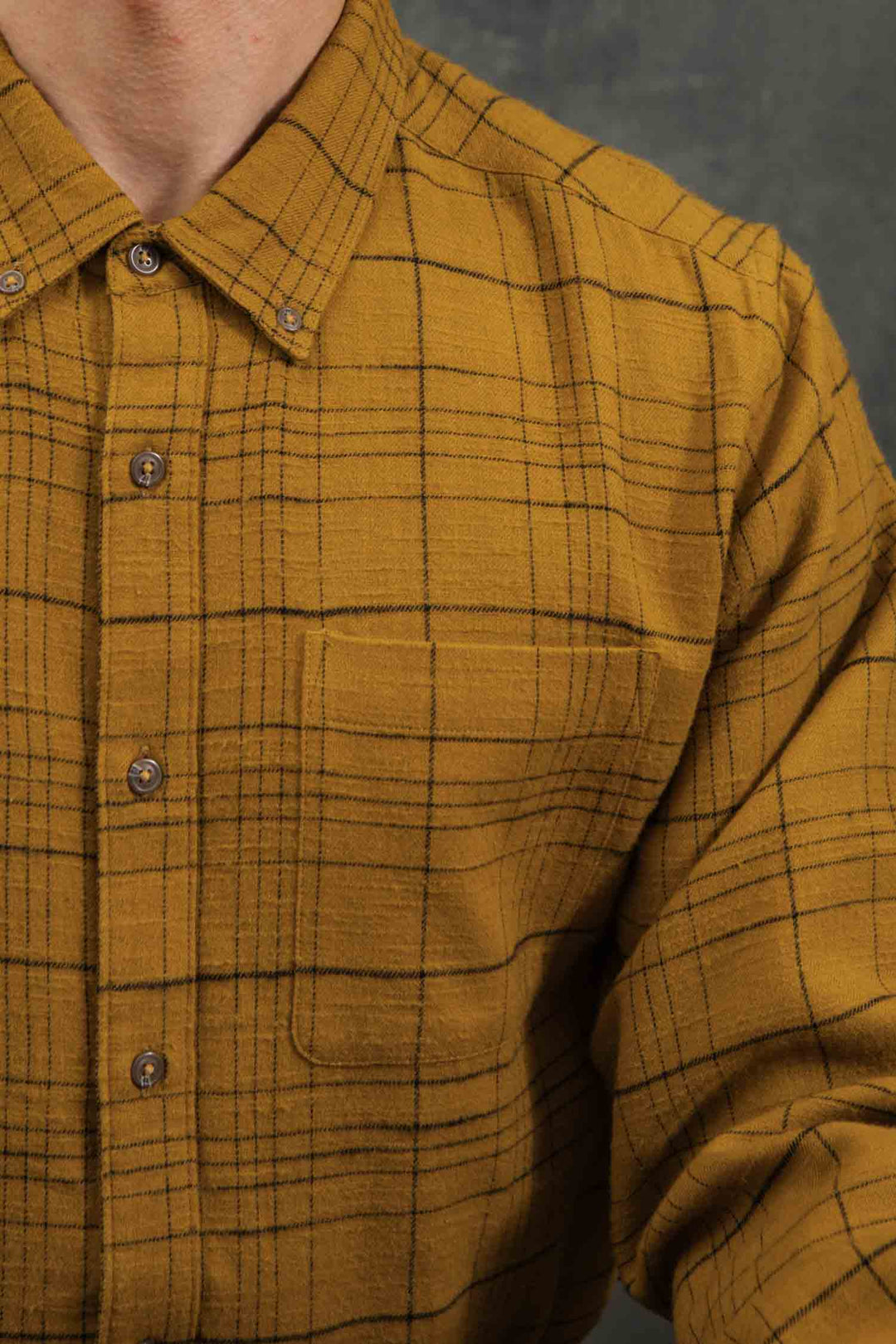 A close-up of a person wearing the Bridge & Burn Sutton Slim Shirt in Golden Horizon Plaid, shown from shoulders to mid-torso against a dark background.
