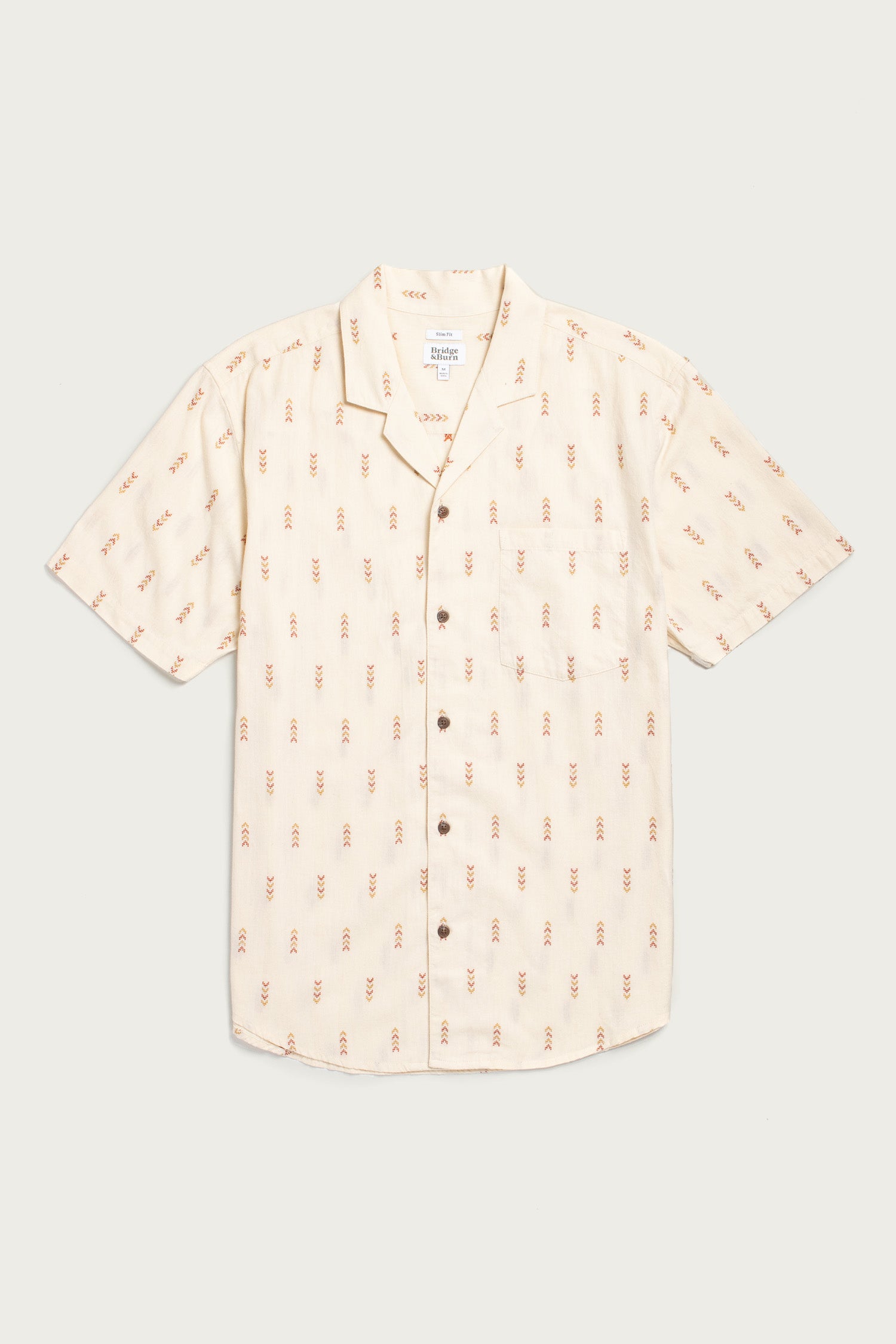 The Bridge & Burn Collins Slim Shirt in Dune Chevron is a cream, summerweight cotton button-up with a camp collar, red and brown geometric print, and single chest pocket, shown laid flat on a light background.