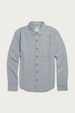 The Bridge & Burn Sutton Slim Shirt in Denim Twill is a light blue, long-sleeve recycled cotton shirt with a chest pocket, buttoned collar, and dark buttons, featuring a minimalist design and laid flat on a white background.