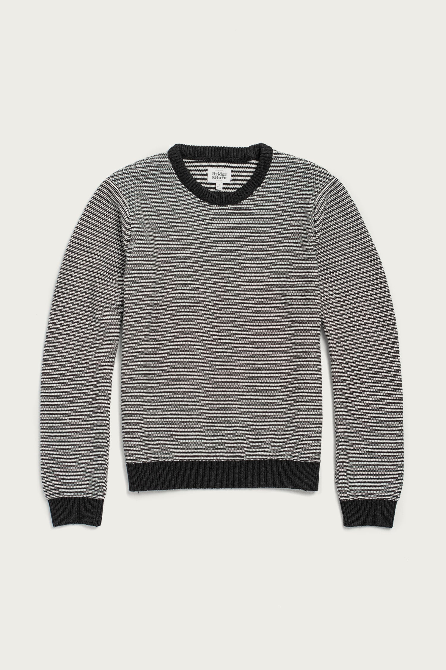 The Ansel Sweater by Bridge & Burn is a sustainable mid-weight crew neck with charcoal and white stripes, finished with solid black cuffs, collar, and hem. Shown here in a long-sleeve style on a white background.