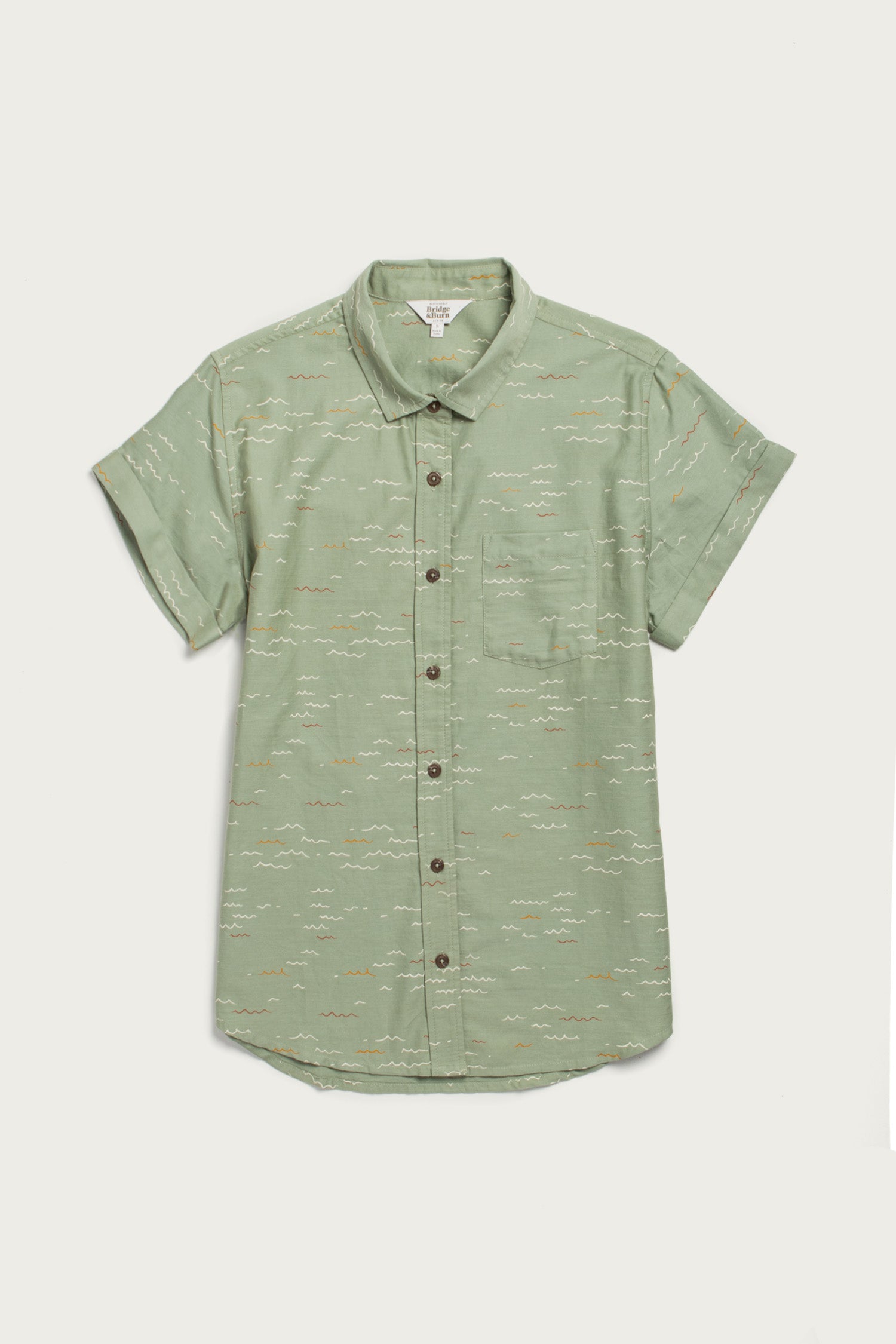 The Bridge & Burn Bea Shirt in Teal Tide Waves is a light green classic, crafted from organic cotton with short sleeves, a front pocket, and subtle white and brown wave patterns—shown on an off-white background.