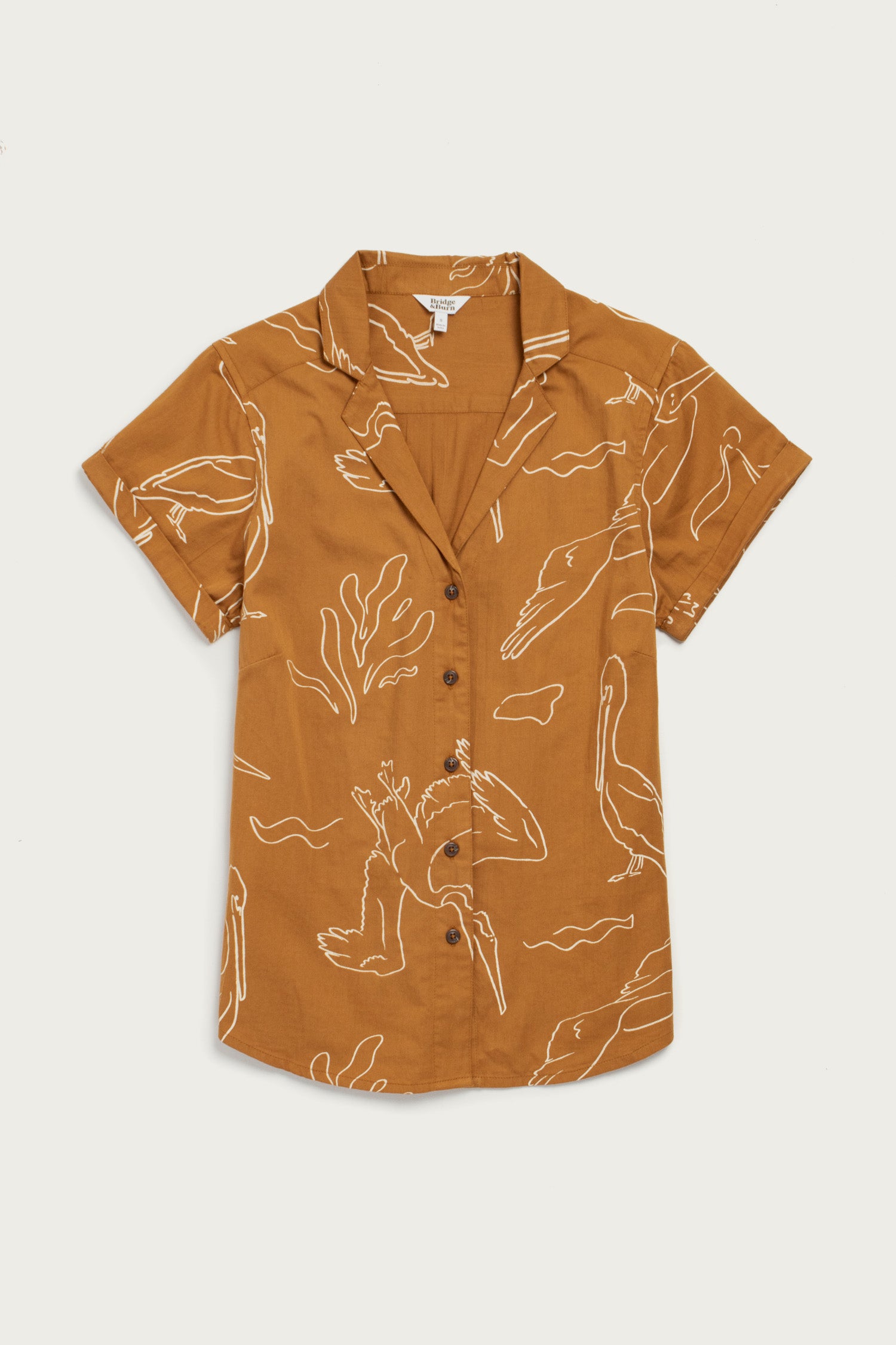 The Bridge & Burn Innes Shirt / Shoreflight is a relaxed fit, short sleeve brown button-up featuring a white pelican and abstract pattern, crafted from soft organic cotton and shown laid flat on a plain white background.