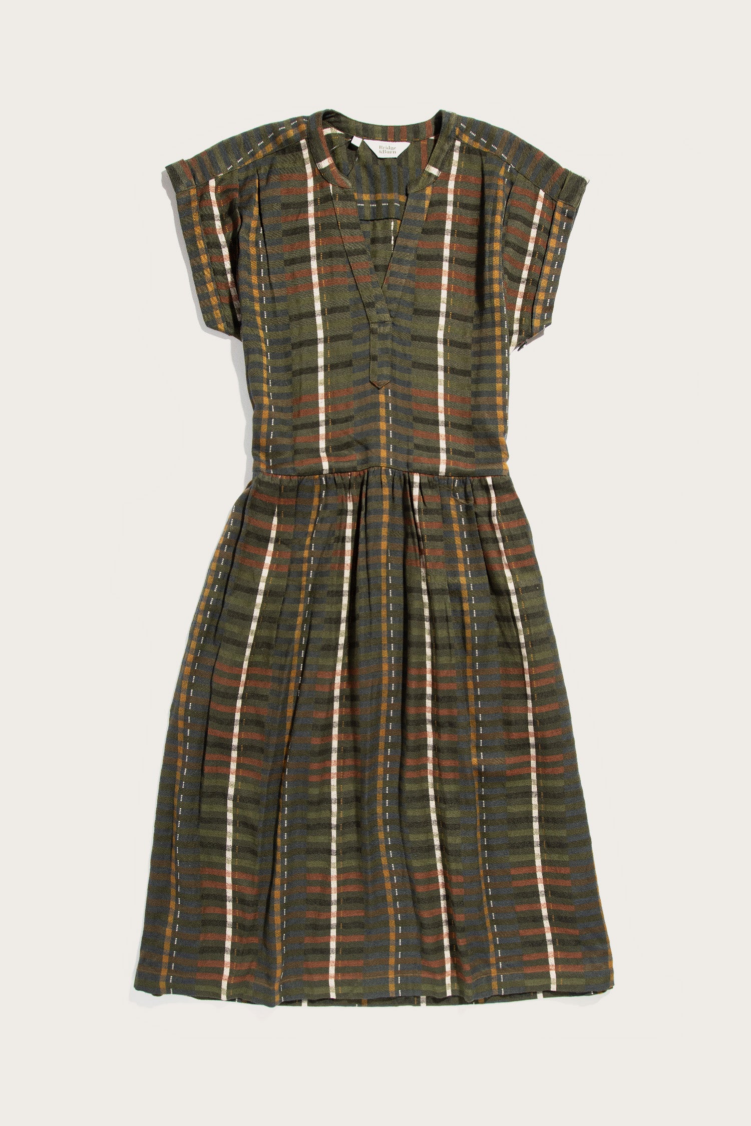 The Ira Dress in Olive Stripe by Bridge & Burn is a wrinkle-resistant, knee-length pullover with short sleeves, buttoned front, and fitted waist. It features brown, white, and orange vertical stripes on a green base with a pleated skirt.