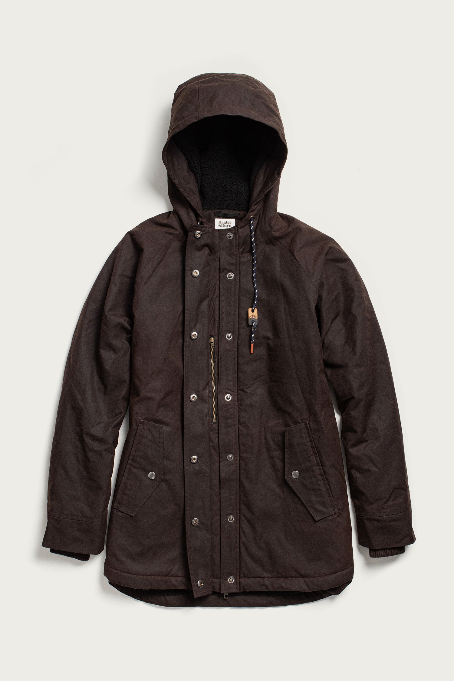 The Bridge & Burn Sequoia Parka in umber waxed canvas features a hood with drawstring, snap buttons, front zipper, two large flap pockets, and fleece lining, shown laid flat on a light background.