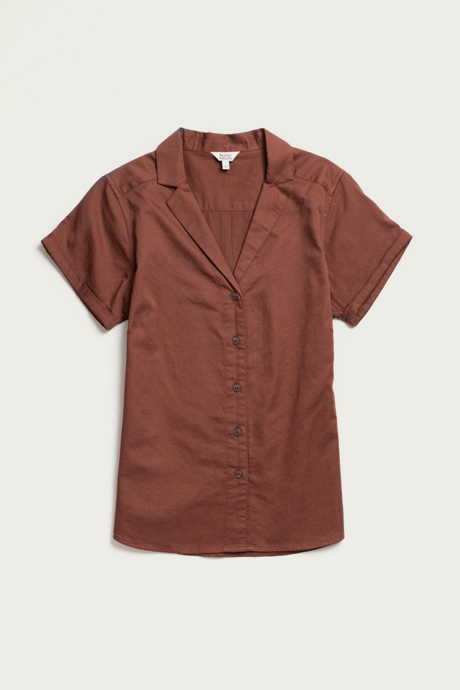 The Bridge & Burn Innes Shirt in Copper is a relaxed fit, short-sleeve button-up blouse with a notched collar, crafted from organic cotton and shown laid flat on a white background.