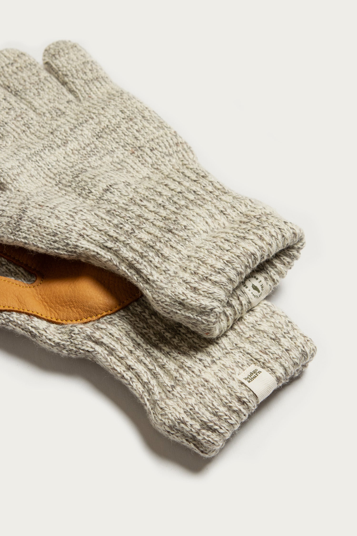 Bridge & Burn’s Ragg Wool Lined Glove in Oatmeal is shown on a light surface, with brown leather palm lining visible inside one glove and a small white tag attached to the cuff.