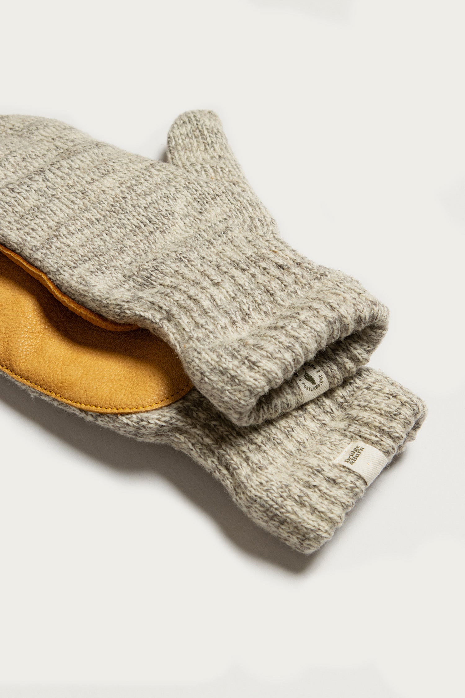 Bridge & Burn's Ragg Wool Lined Mitten in Oatmeal features a textured gray knit and a tan leather palm patch, shown overlapping on a plain white background.