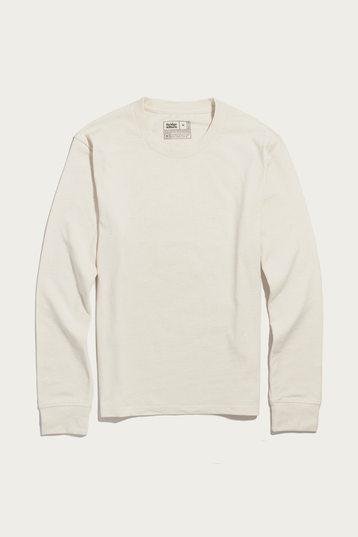 The Bridge & Burn Barney Long Sleeve Tee in Ivory, a relaxed fit crew neck shirt with long sleeves, is laid flat on a white background. Made from recycled cotton, it features visible cuffs and a neck tag.