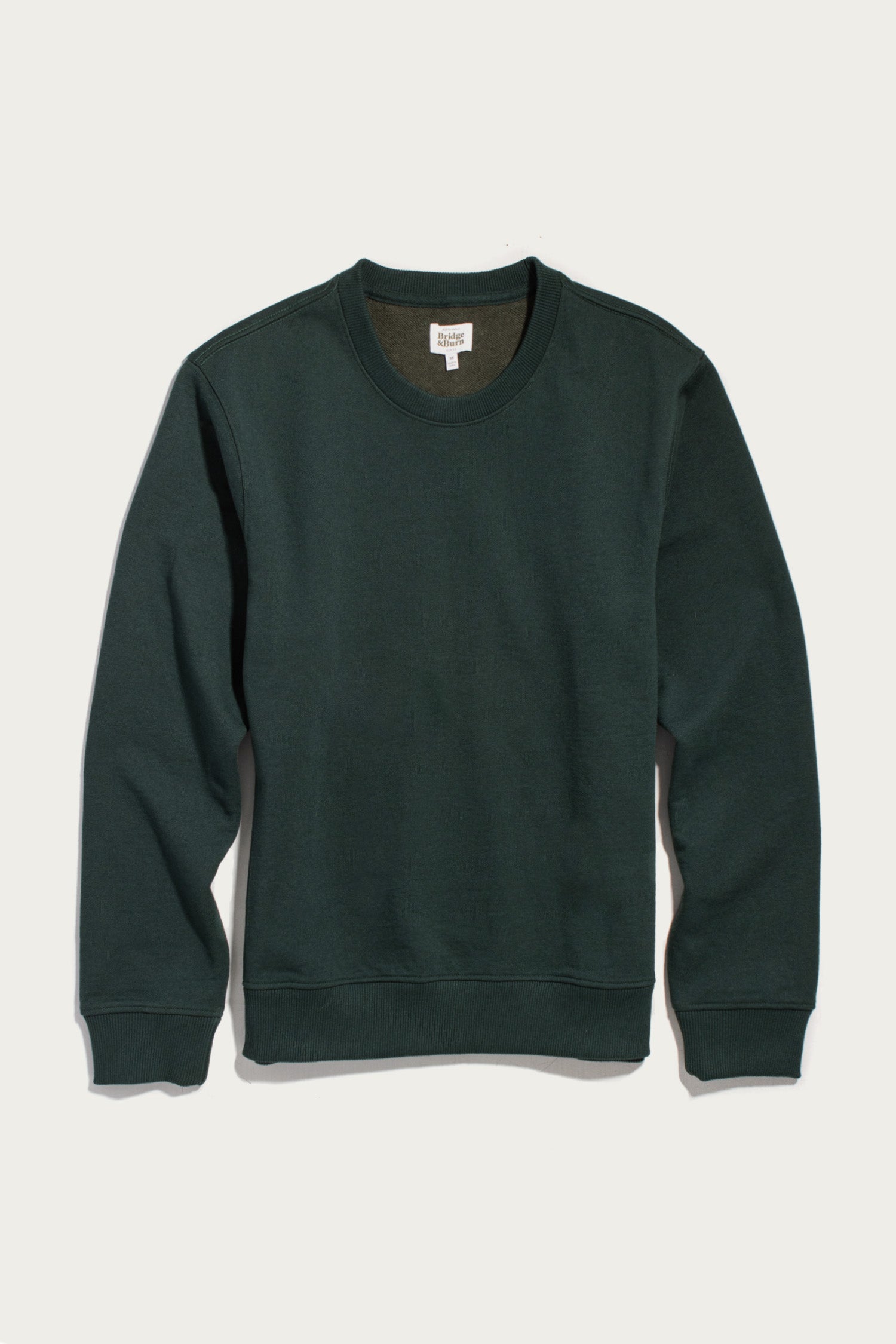 A Hayden Crew Sweatshirt in Juniper by Bridge & Burn, featuring a dark green hue, crew neck, and long sleeves, crafted from recycled cotton and displayed flat on a white background.