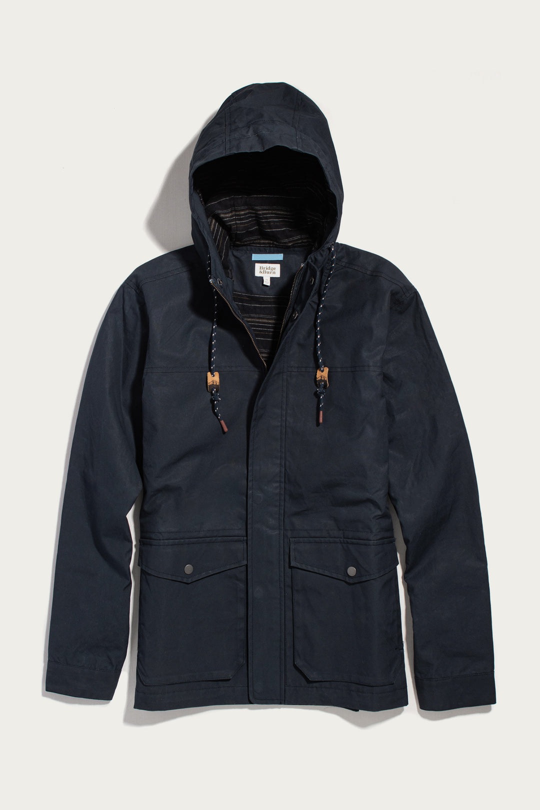 Bridge & Burn Marshall Jacket in navy waxed canvas, featuring a hood, two front flap pockets, and a striped lining.