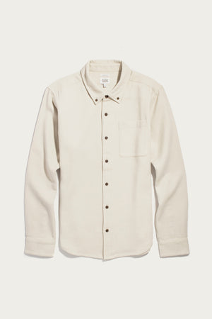 The Bridge & Burn Sutton Slim Shirt in Fawn Flannel is a slim-fit, long-sleeve shirt crafted from cream-colored organic cotton with a soft flannel texture. It features a single chest pocket, dark buttons, and is showcased on a plain white background for a clean, minimalist look.