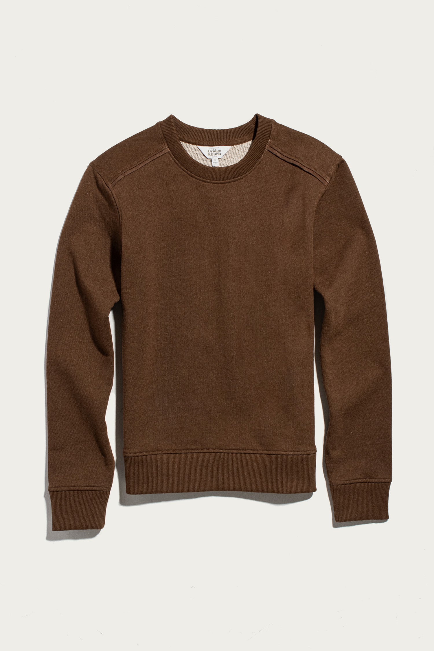 The Bailey Crew Sweatshirt in Cumin by Bridge & Burn is laid flat on a white background. This sustainable crewneck long-sleeve sweatshirt features ribbed cuffs, hem, and neckline, with visible stitching along the shoulders and sides.