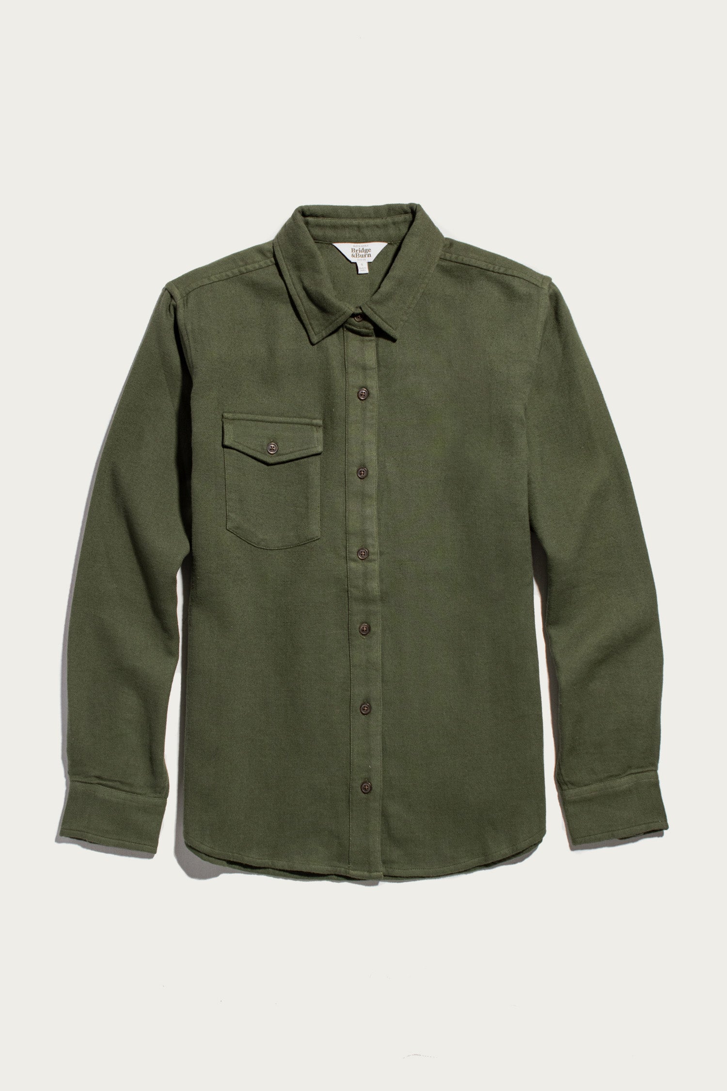 The Bird Shirt / Pine Flannel by Bridge & Burn features an olive green hue in a relaxed fit, crafted from organic cotton flannel. This long-sleeve shirt includes a collared neckline and a single chest pocket on the left side, and is showcased against a plain white background.