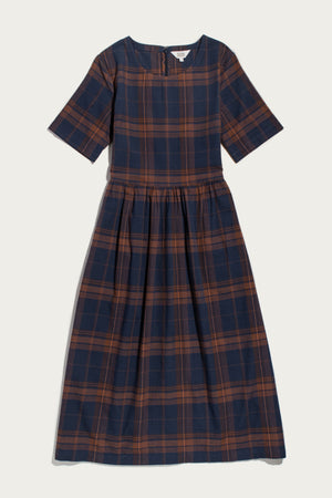 Introducing the Perry Dress in Cinder Plaid from Bridge & Burn—a midi-length dress crafted from organic cotton, featuring short sleeves, a round neckline, and a navy blue and brown plaid pattern. The gathered waist creates a subtly flared skirt for an effortlessly flattering silhouette.