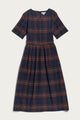 Introducing the Perry Dress in Cinder Plaid from Bridge & Burn—a midi-length dress crafted from organic cotton, featuring short sleeves, a round neckline, and a navy blue and brown plaid pattern. The gathered waist creates a subtly flared skirt for an effortlessly flattering silhouette.