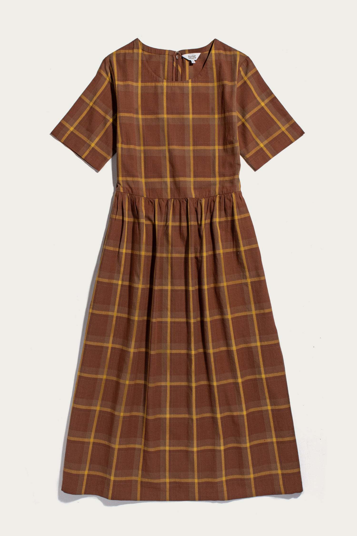 The Perry Dress in Harvest Plaid by Bridge & Burn is an organic cotton midi-length dress featuring a brown and yellow plaid pattern, short sleeves, a round neckline, fitted bodice, gathered waist, and a flowing gathered skirt, shown laid flat against a light background.