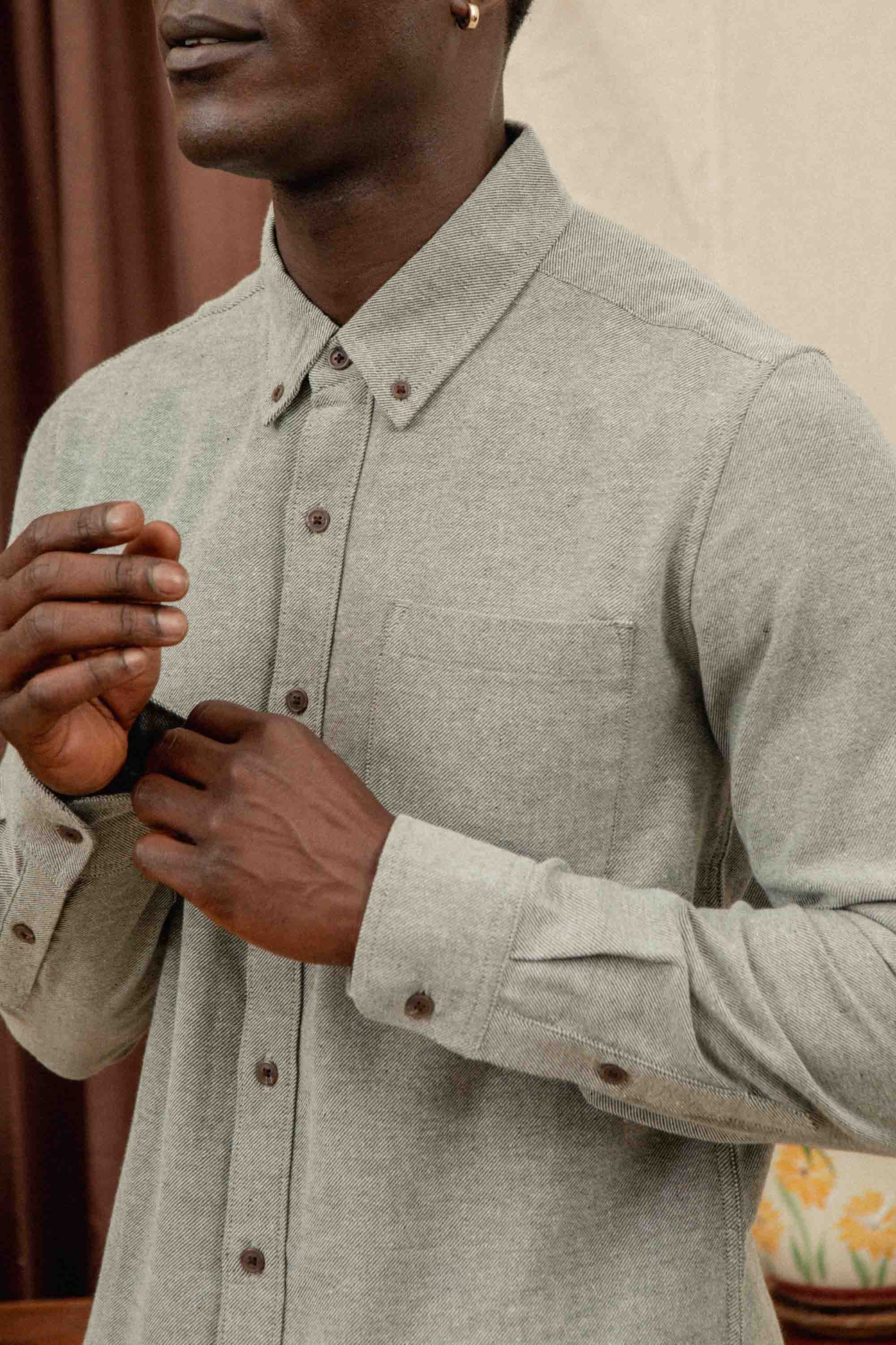 A person wearing the Bridge & Burn Sutton Slim Shirt in Olive Twill stands indoors, adjusting their sleeve cuff. Only their upper body is visible.