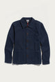 The Bridge & Burn Men’s Studio Chore Coat in Indigo is inspired by classic chore coat design, featuring a collar, chest pocket, and two large front pockets. Crafted from organic cotton, it is displayed on a white background.