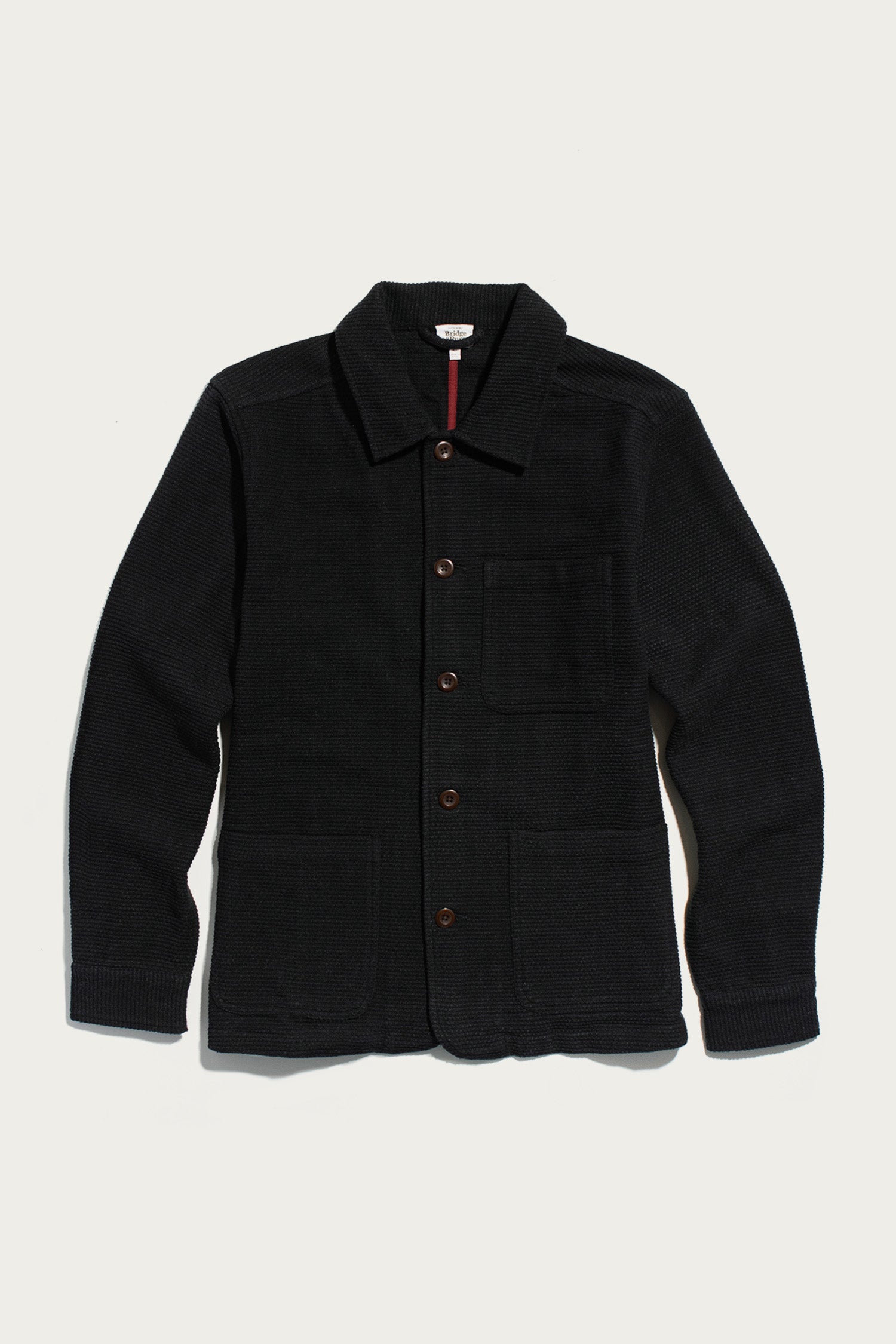 The Men’s Studio Chore Coat in Washed Black by Bridge & Burn, featuring a chore coat-style button-up design with a collar and three front pockets, is laid flat on a white background.