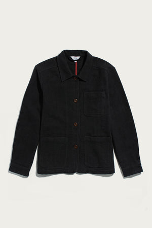 The Women’s Studio Chore Coat by Bridge & Burn in washed black—crafted from organic cotton—features a collar, three front pockets, and brown buttons, shown laid flat on a white background.