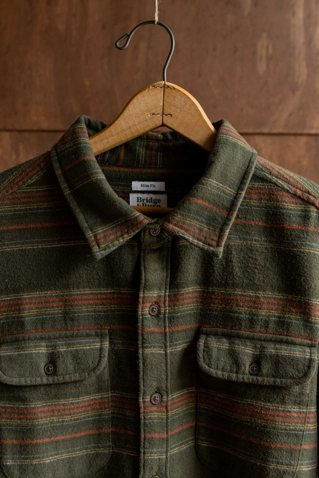Bridge & Burn Cole Slim Shirt in olive green brushed cotton with horizontal rust, teal, and yellow stripes, featuring two chest pockets and a button-down collar.