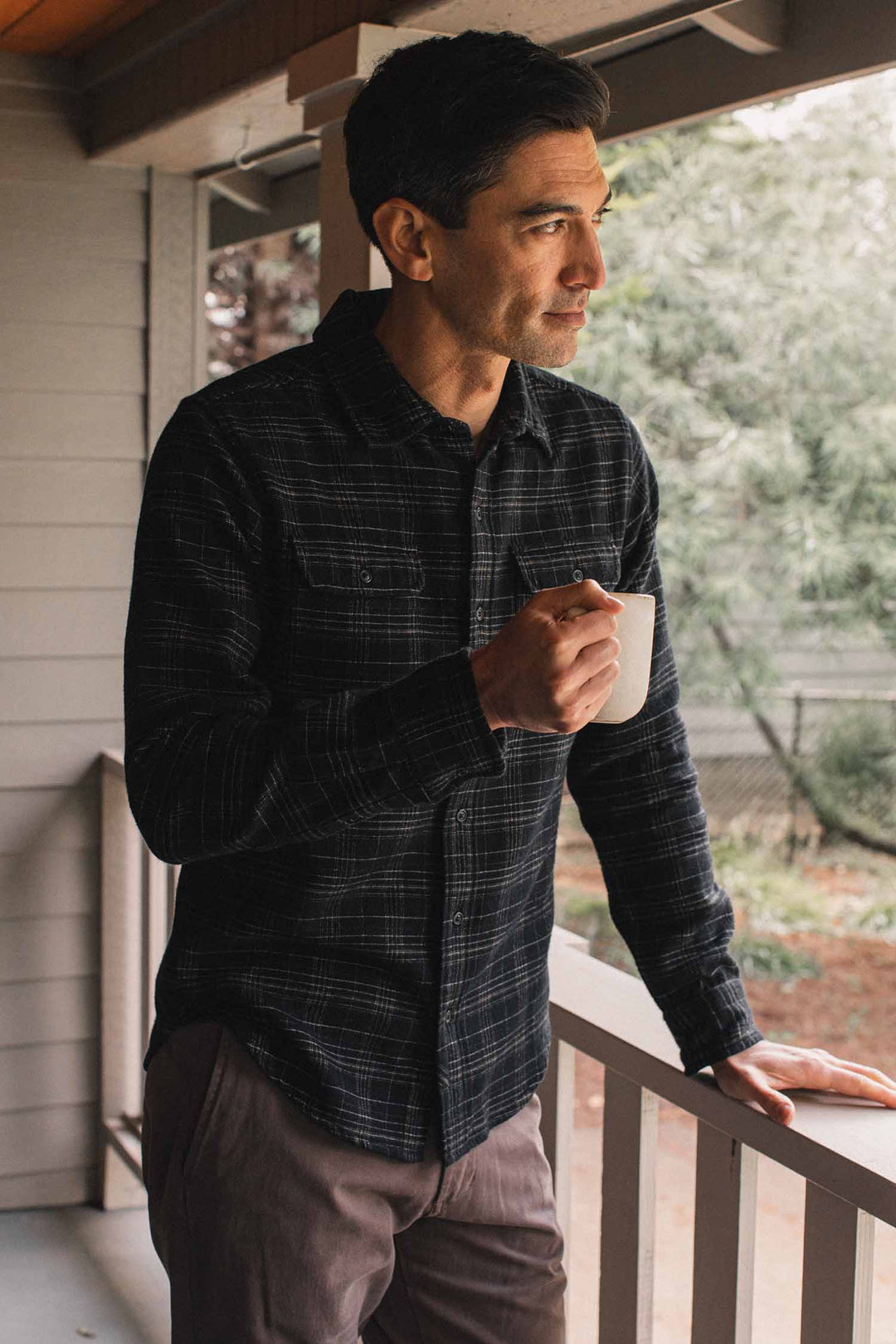 Man in a Bridge & Burn Cole Slim Shirt / Obsidian Grid standing on a porch holding a mug.