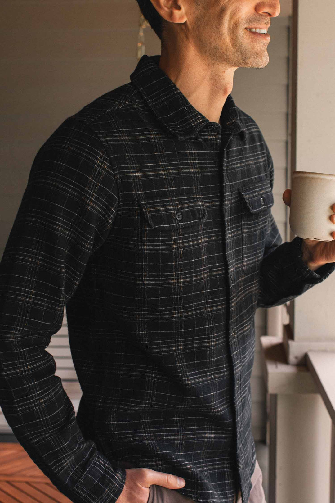A man wears a Bridge & Burn Cole Slim Shirt / Obsidian Grid, a slim fit, black button-down with a subtle tan grid pattern, while holding a ceramic mug.