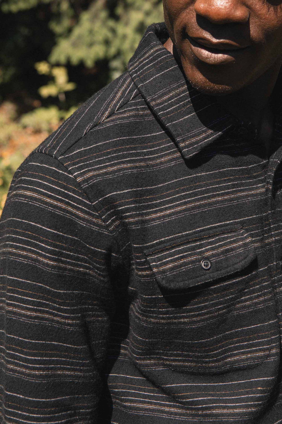 Close-up of a man wearing a Bridge & Burn Cole Slim Shirt / Raven Stripe in black with thin, horizontal stripes in white and copper.