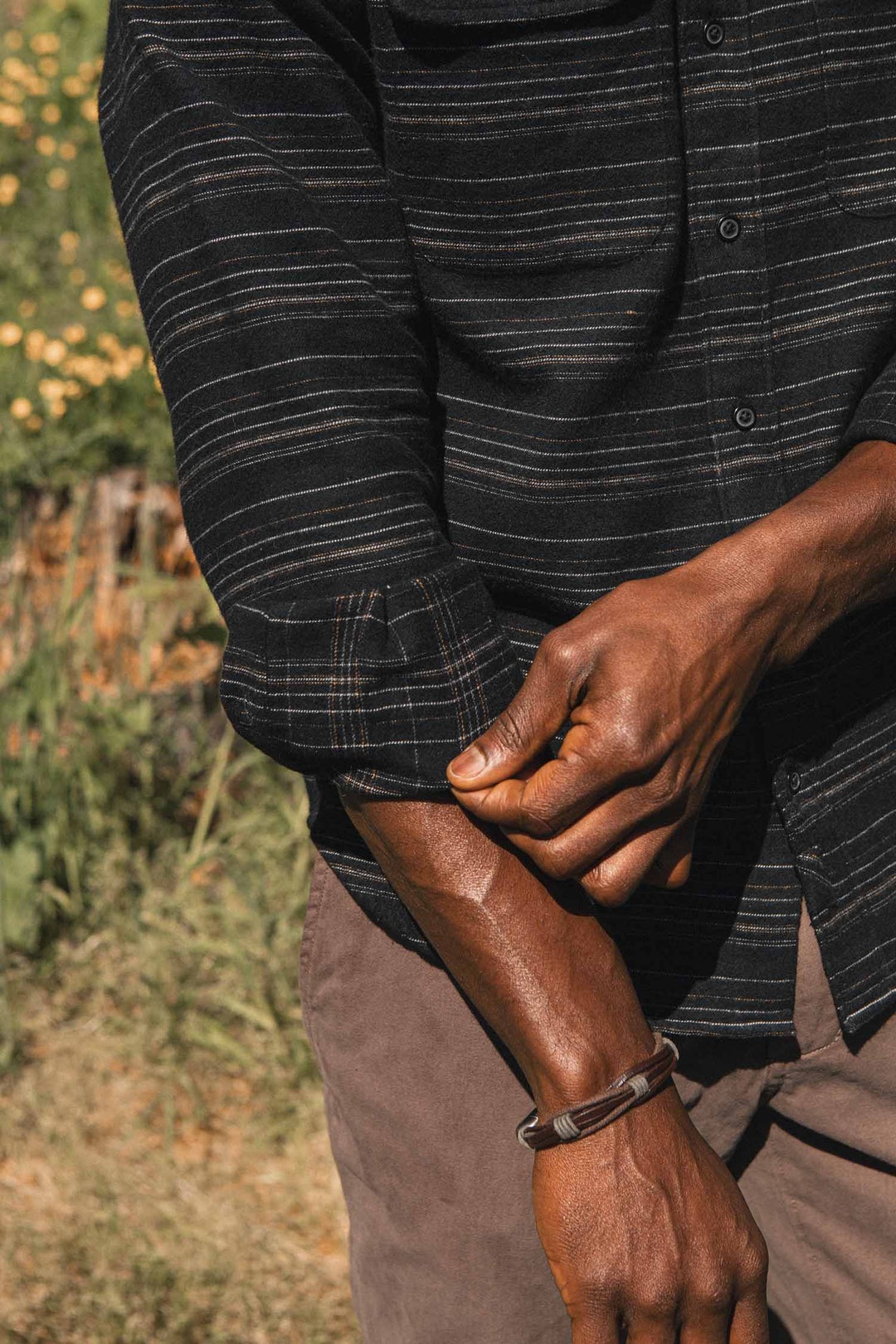 A person rolls up the sleeve of a black, slim-fit Cole Slim Shirt / Raven Stripe button-down with thin horizontal stripes.