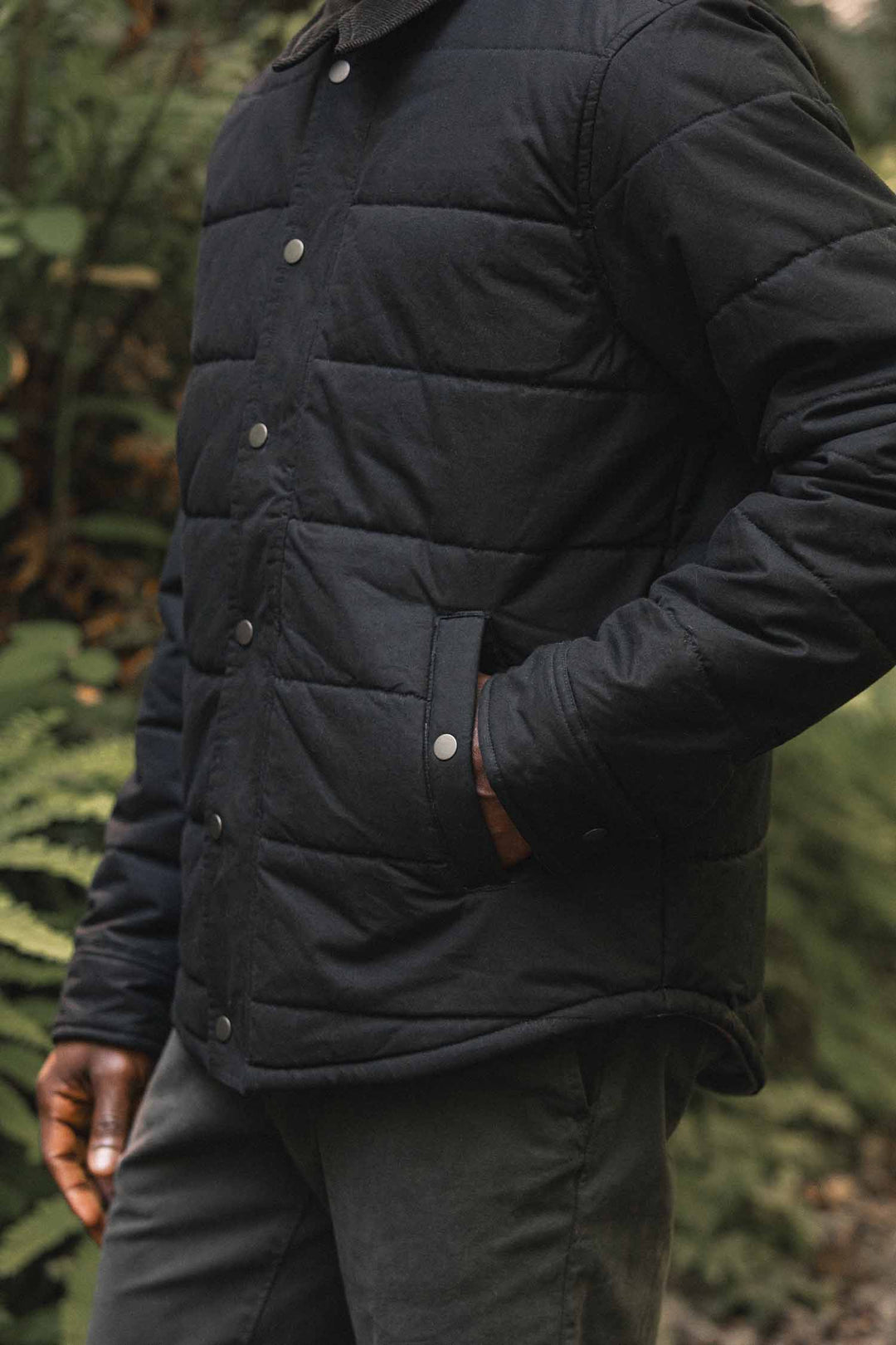 A person wearing a black Bridge & Burn Holman Quilted Jacket / Black Canvas featuring snap-button closures and front pockets.