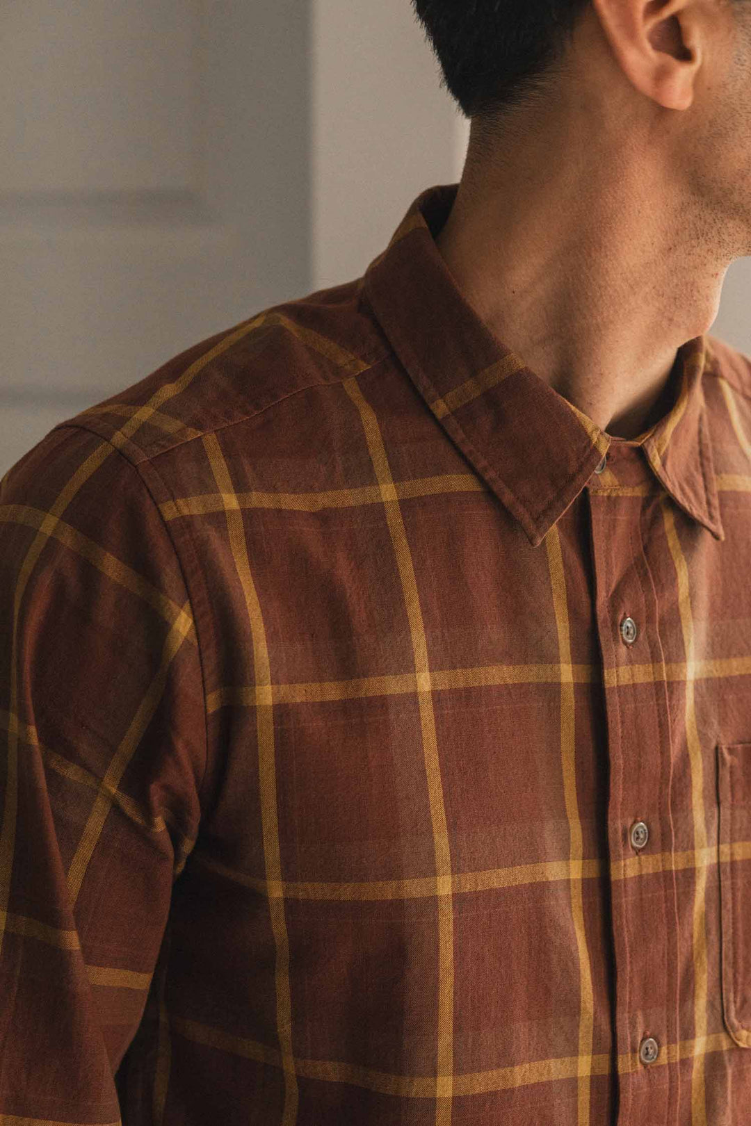 A person wearing the Bridge & Burn Larson Shirt in Harvest Plaid—a brown brushed flannel button-up—looks to the right, with their face not visible.